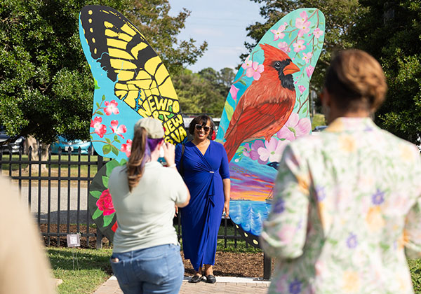 Woman in blue dress posing by a large, colorful butterfly wing mural at Huntington Park Botanical Garden.
